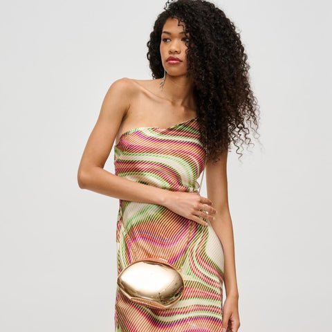 Woman in a printed one-shoulder maxi dress and gold clutch for NYE