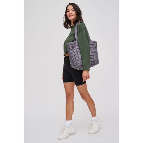 Woman in black biker shorts & green sweatshirt carrying a quilted tote in gray